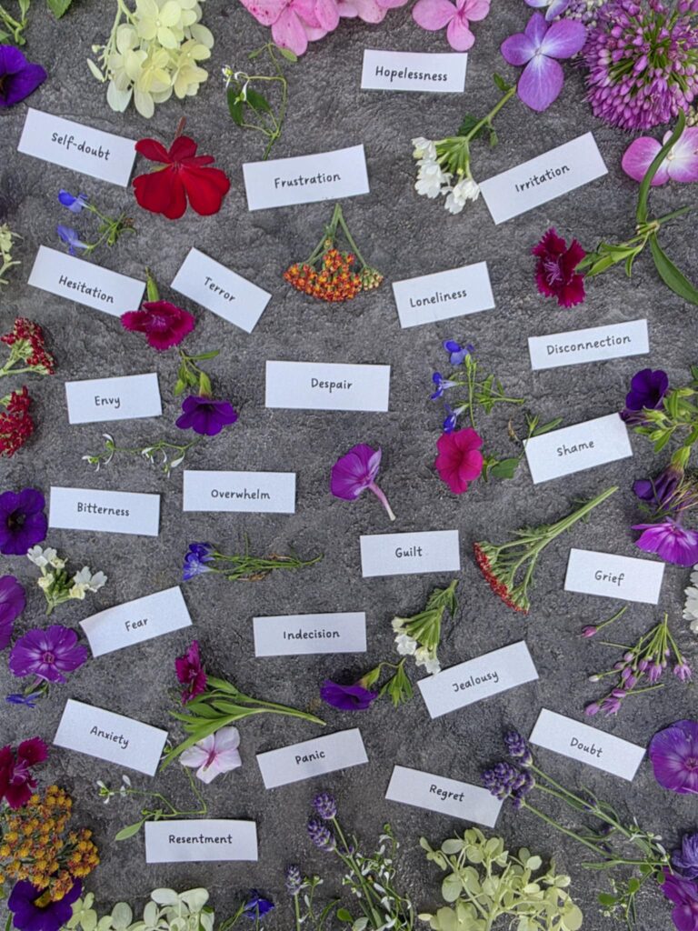 Papers labeled with negative emotions surrounded by a variety of fresh flowers, symbolizing emotional healing through custom flower remedies.